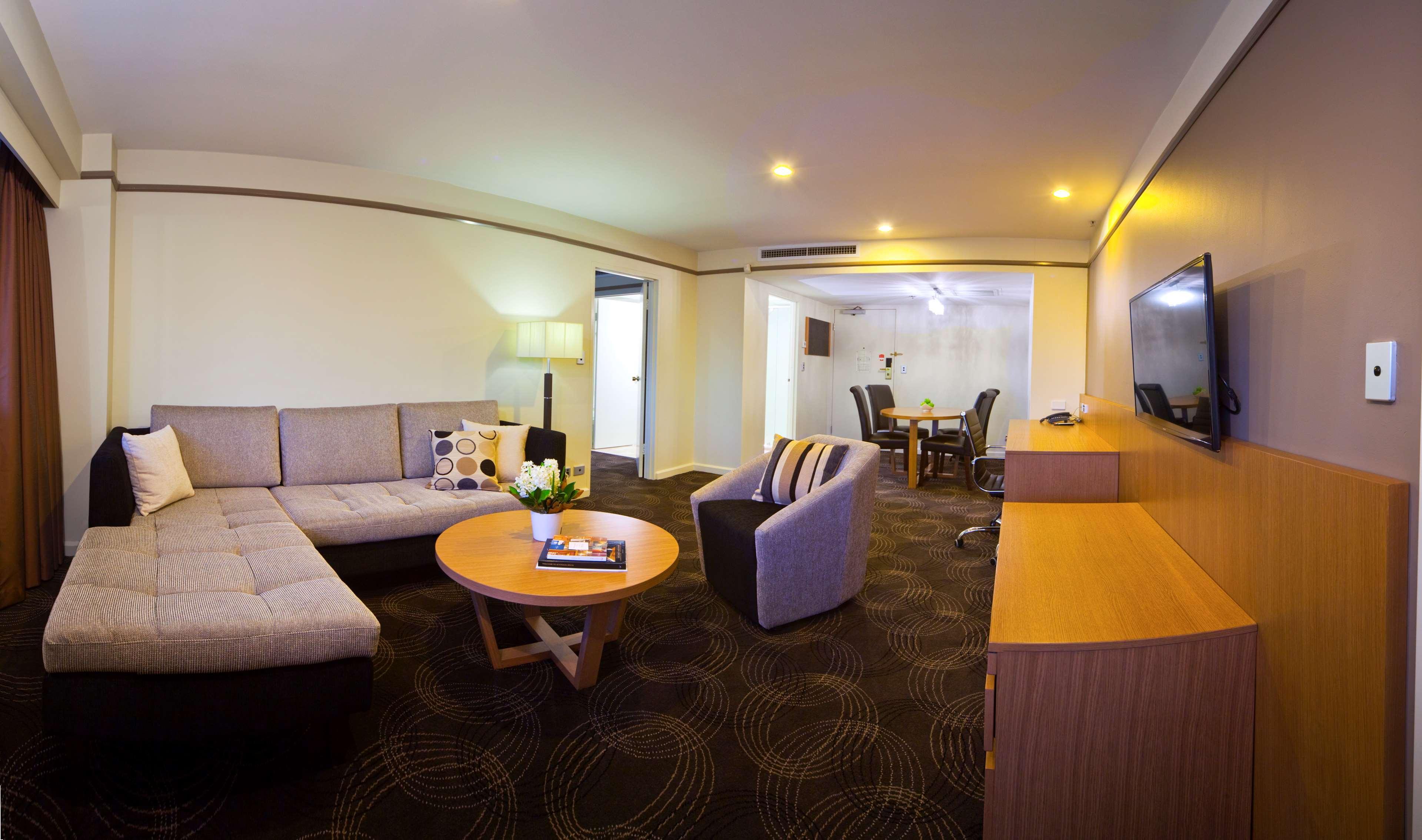 Stamford Plaza Adelaide Hotel Ngoại thất bức ảnh The photo shows a spacious living area with modern decor. On the left, there is a light gray sectional sofa, accompanied by a round wooden coffee table in front of it. A couple of decorative pillows add a touch of color to the sofa. To the right, the
