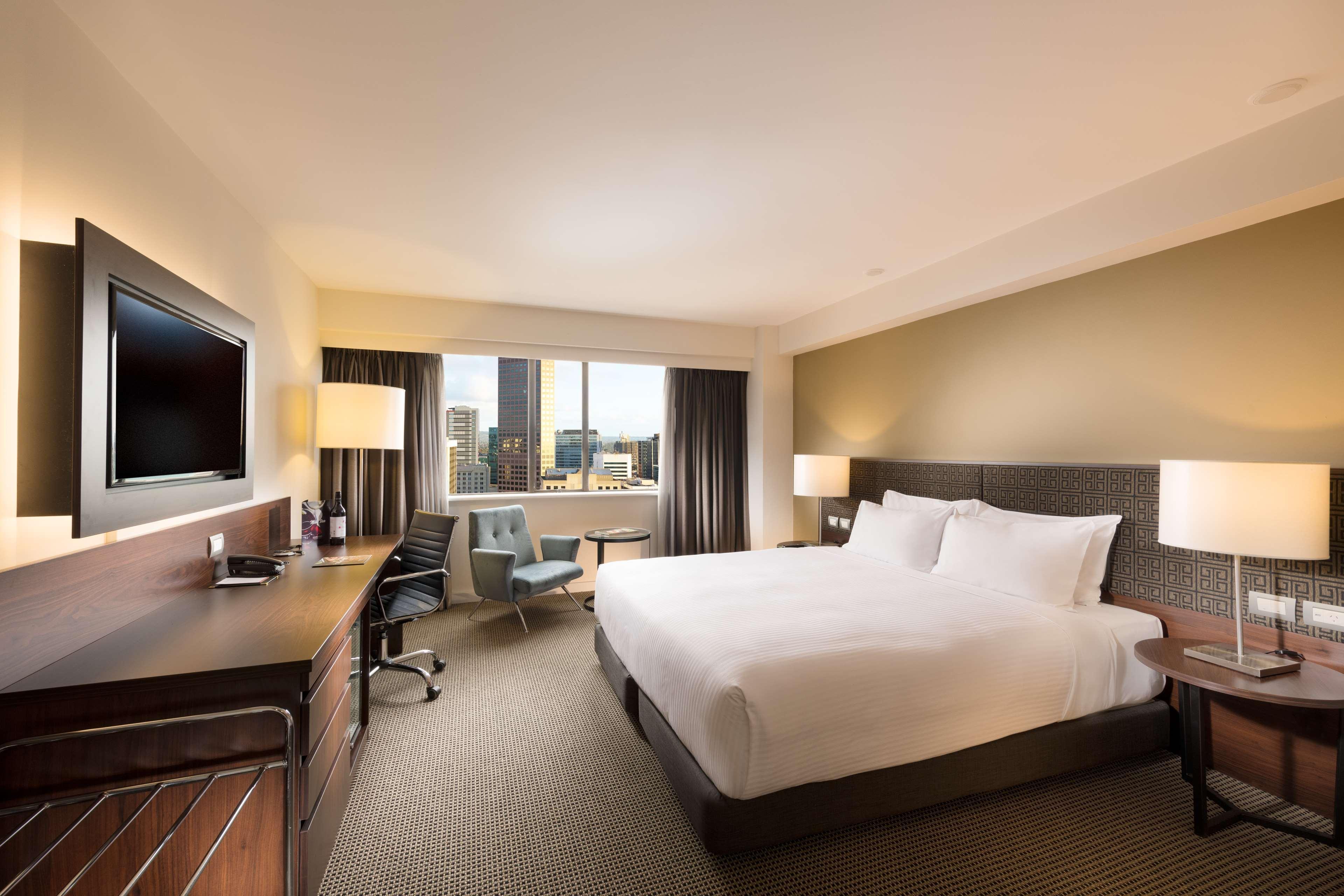 Stamford Plaza Adelaide Hotel Ngoại thất bức ảnh The photo shows a modern hotel room with a contemporary design. It features a large bed with white linens, a bedside table on either side with lamps, and a dark wood accent wall. There's a work desk with an office chair and a flat-screen television m