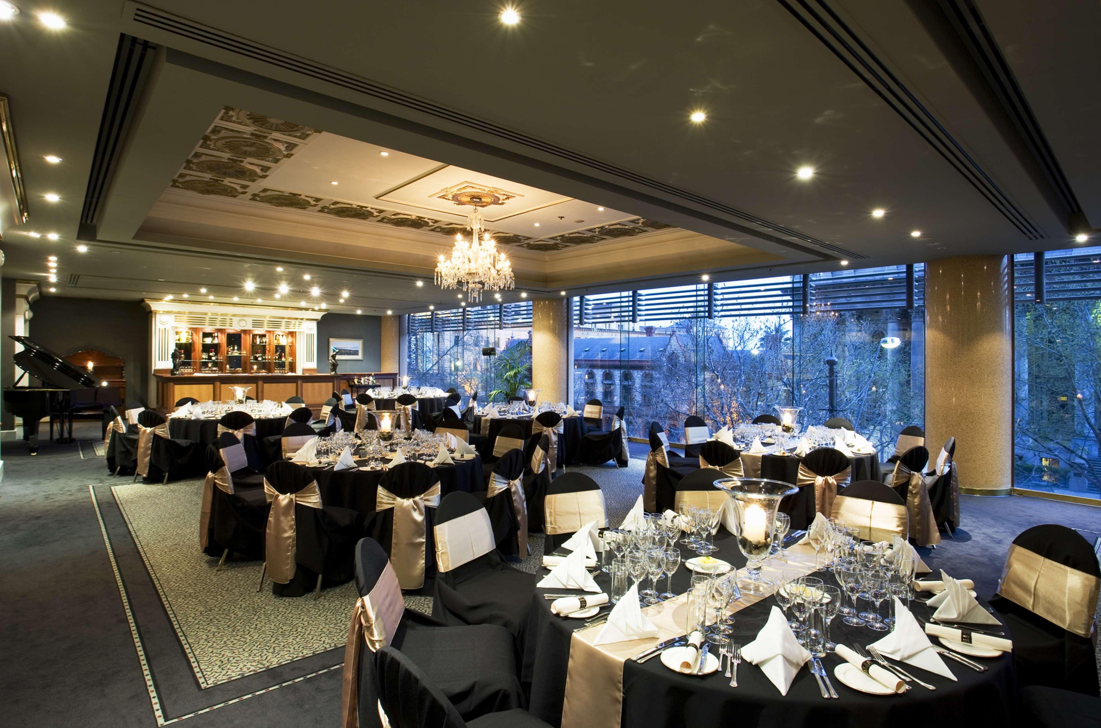 Stamford Plaza Adelaide Hotel Ngoại thất bức ảnh The photo shows an elegant banquet hall or restaurant setting. There are several round tables covered with black tablecloths and adorned with gold accents. Each table is set with fine dining utensils, glassware, and neatly folded napkins. In the back