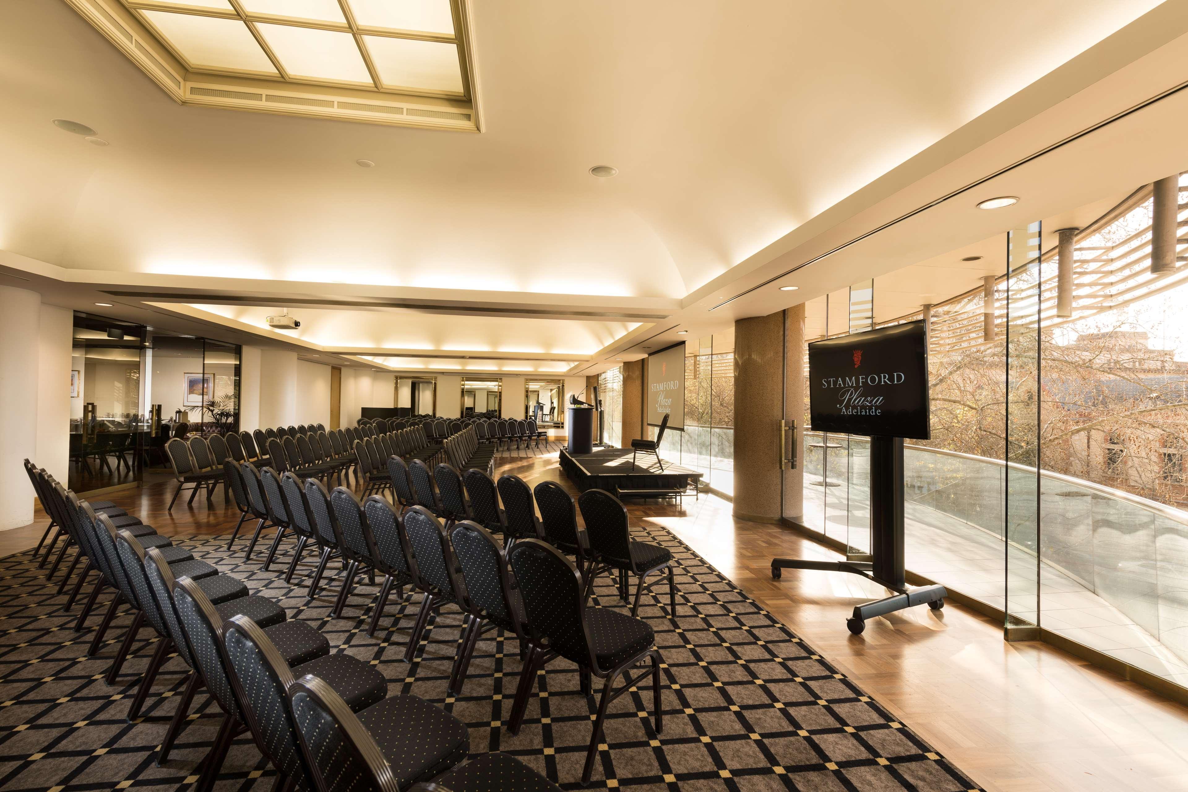 Stamford Plaza Adelaide Hotel Ngoại thất bức ảnh The photo shows a large, elegantly designed event space or meeting room. There are rows of black chairs set up facing a presentation area. The flooring features a patterned carpet, and large windows allow natural light to enter the room. On one side,