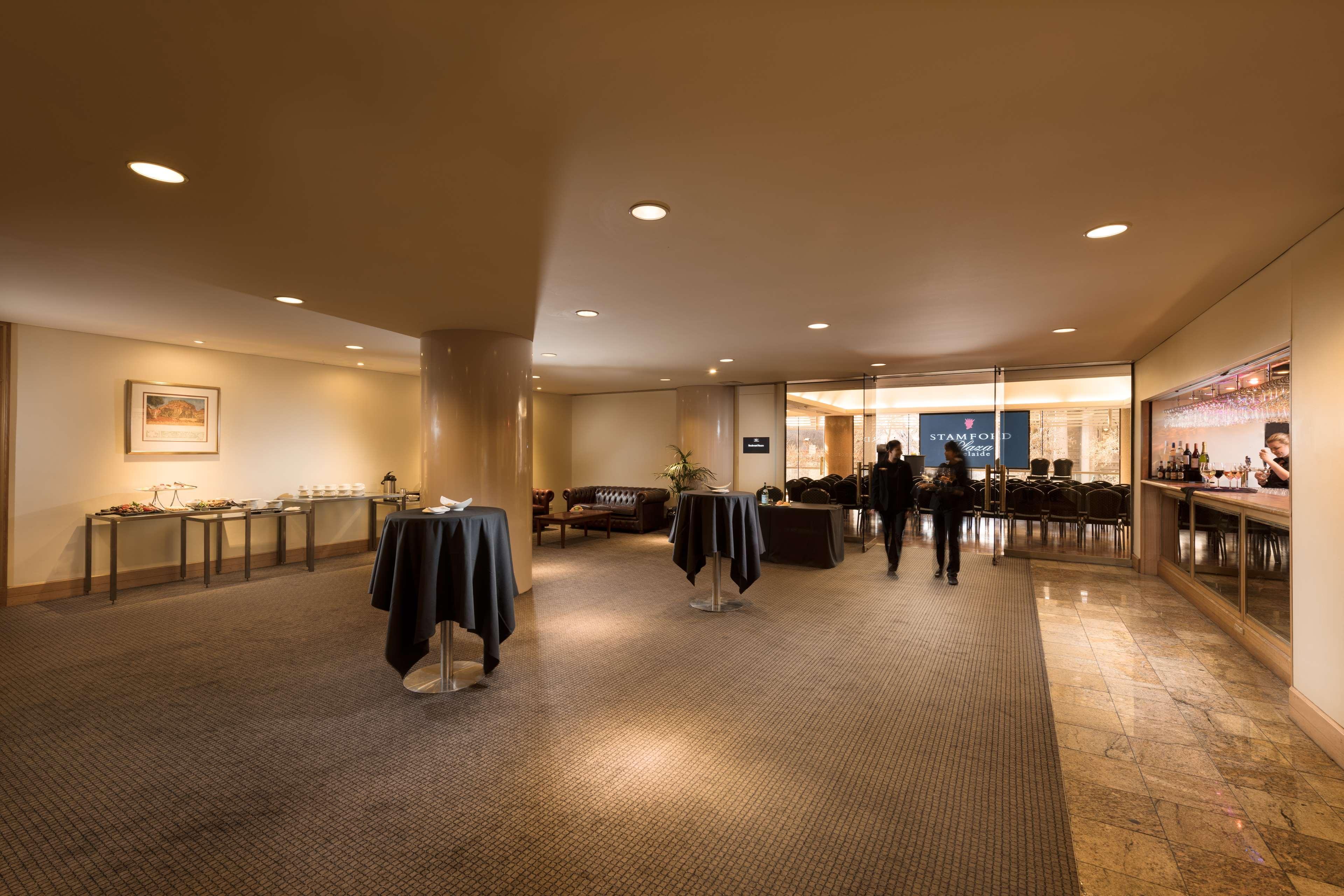 Stamford Plaza Adelaide Hotel Ngoại thất bức ảnh The image shows an indoor space that appears to be a lounge or reception area. There are several round tables with dark tablecloths positioned throughout the room. The floor is carpeted, and the lighting is warm and somewhat dim. In the background, t