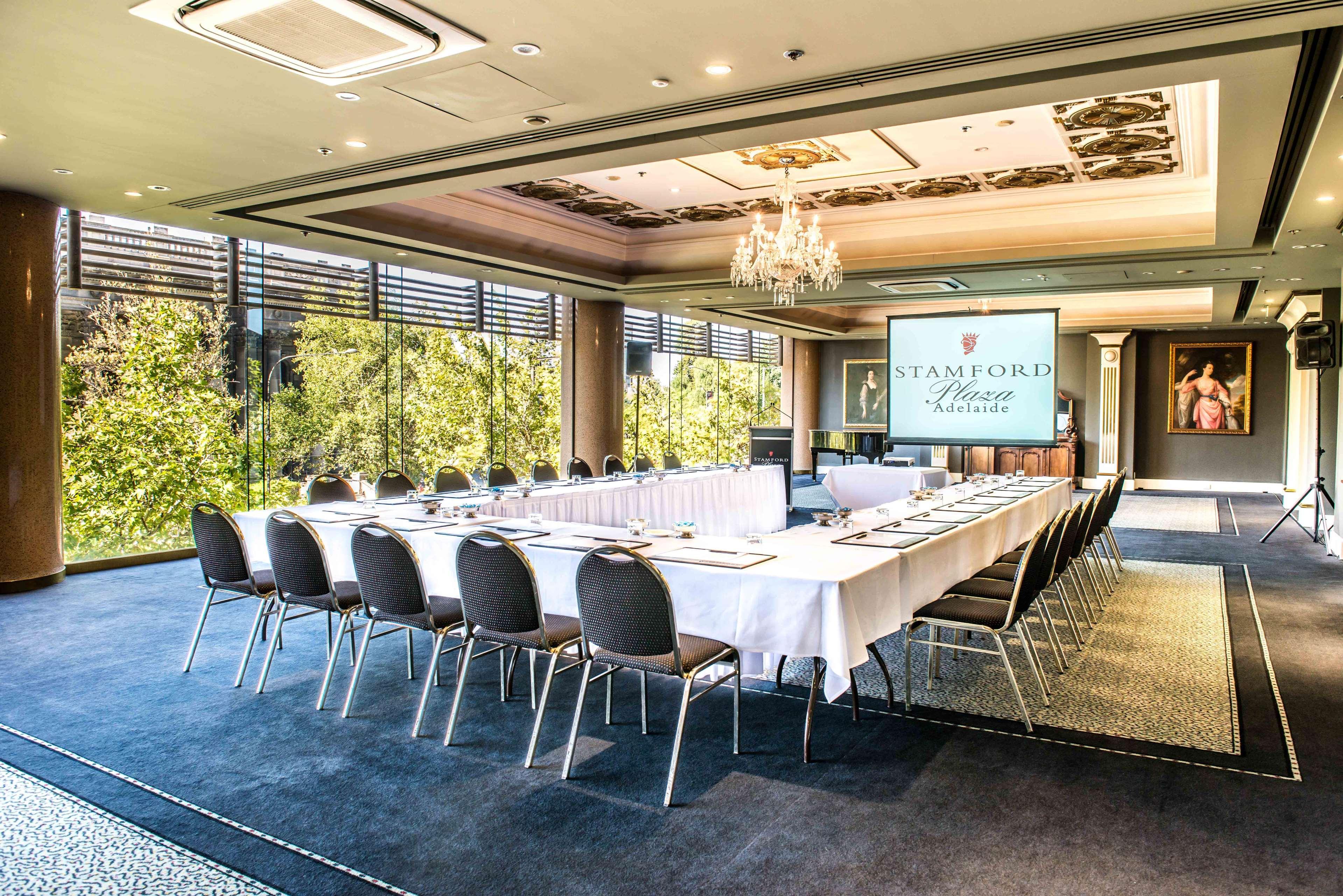 Stamford Plaza Adelaide Hotel Ngoại thất bức ảnh The photo shows a stylish conference room set up for a meeting or event. There is a long rectangular table covered with a white tablecloth, surrounded by black chairs. A large screen displays the name "Stamford" along with a logo. The room features l