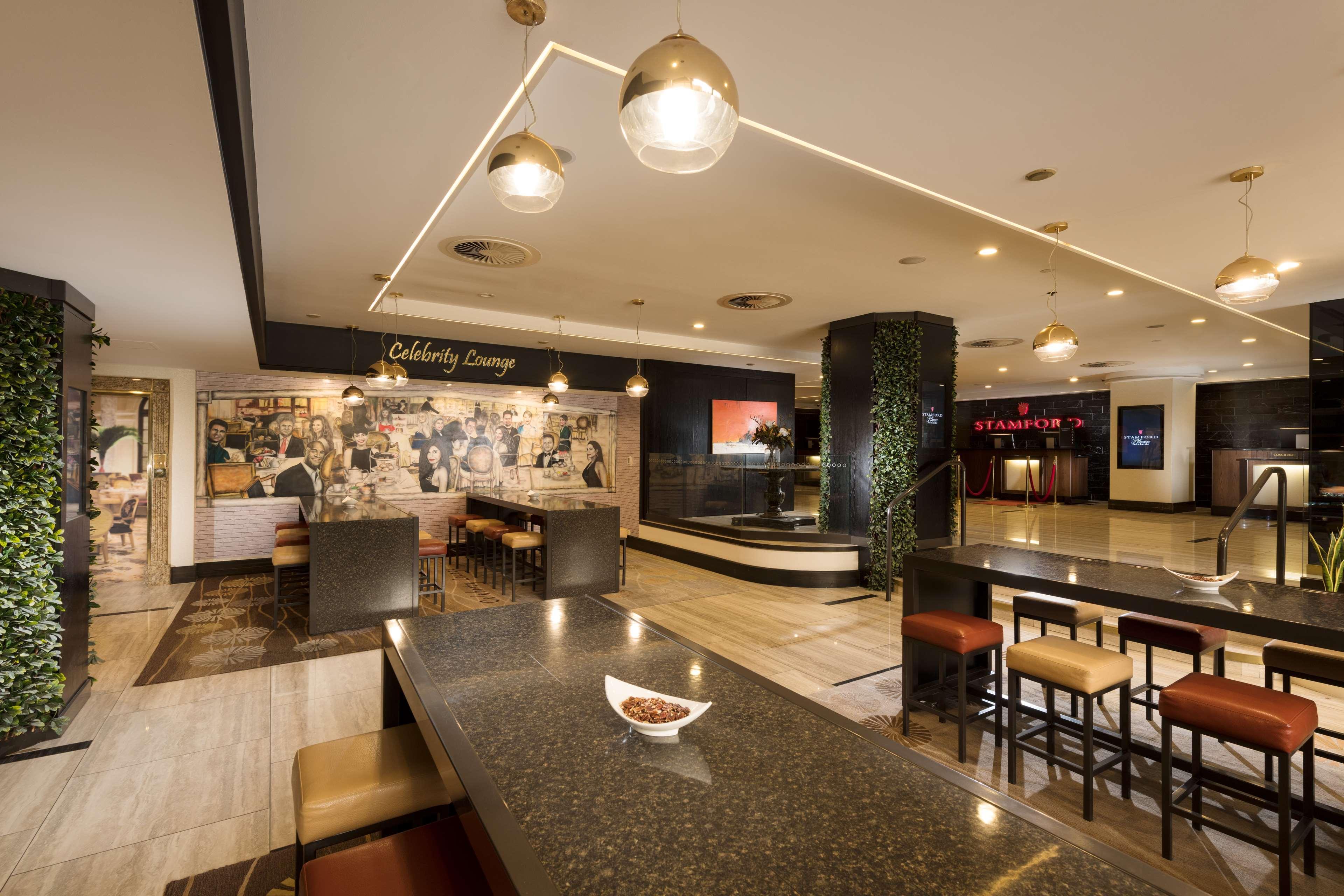 Stamford Plaza Adelaide Hotel Ngoại thất bức ảnh The photo shows a modern and stylish interior of a lounge or restaurant area. Prominent features include a long dark countertop with bar stools, and several pendant lights hanging from the ceiling. In the background, there is a mural or artwork that 
